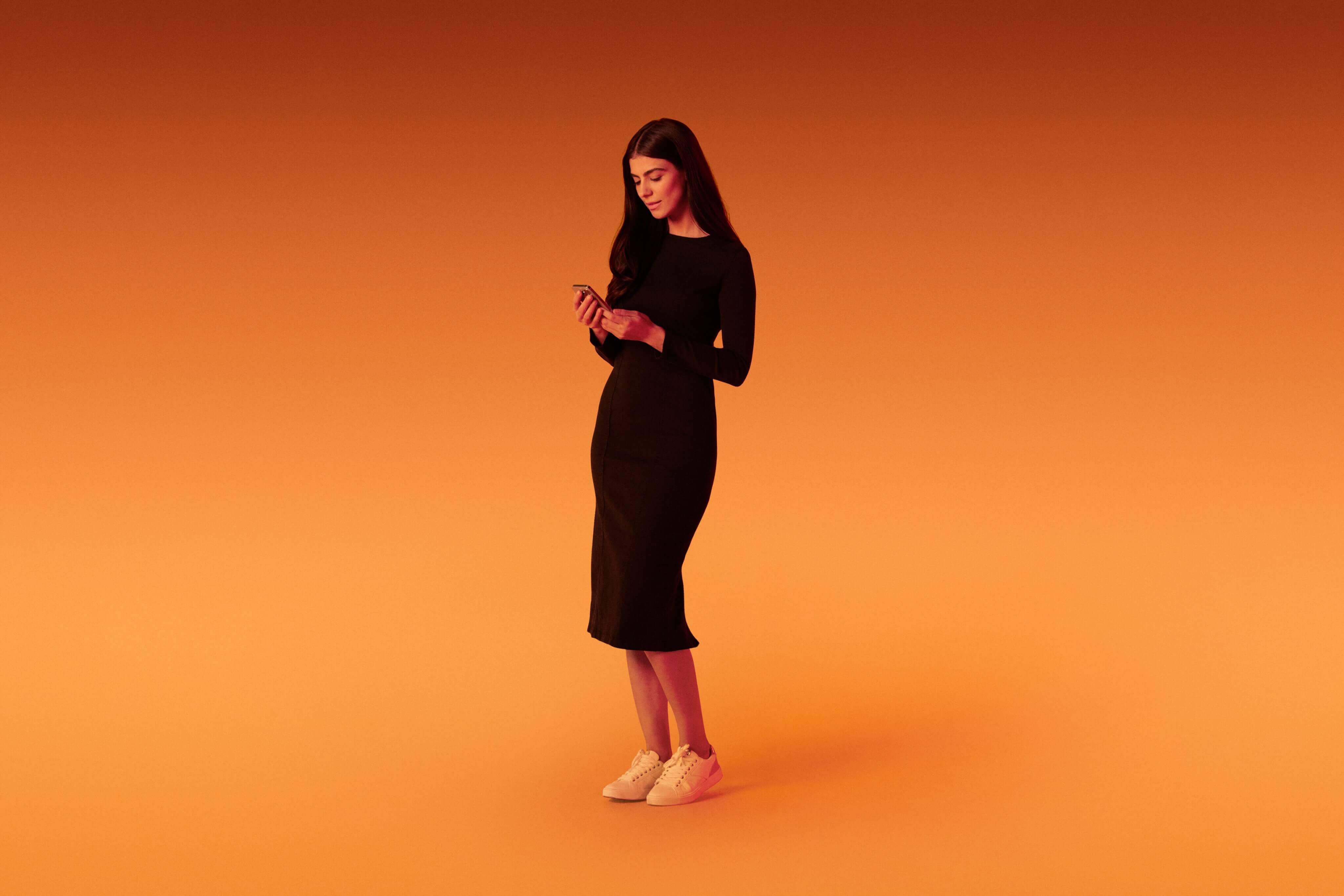 standing woman engaging with the Xapo Bank app on her mobile phone, overlaid with an orange hue.
