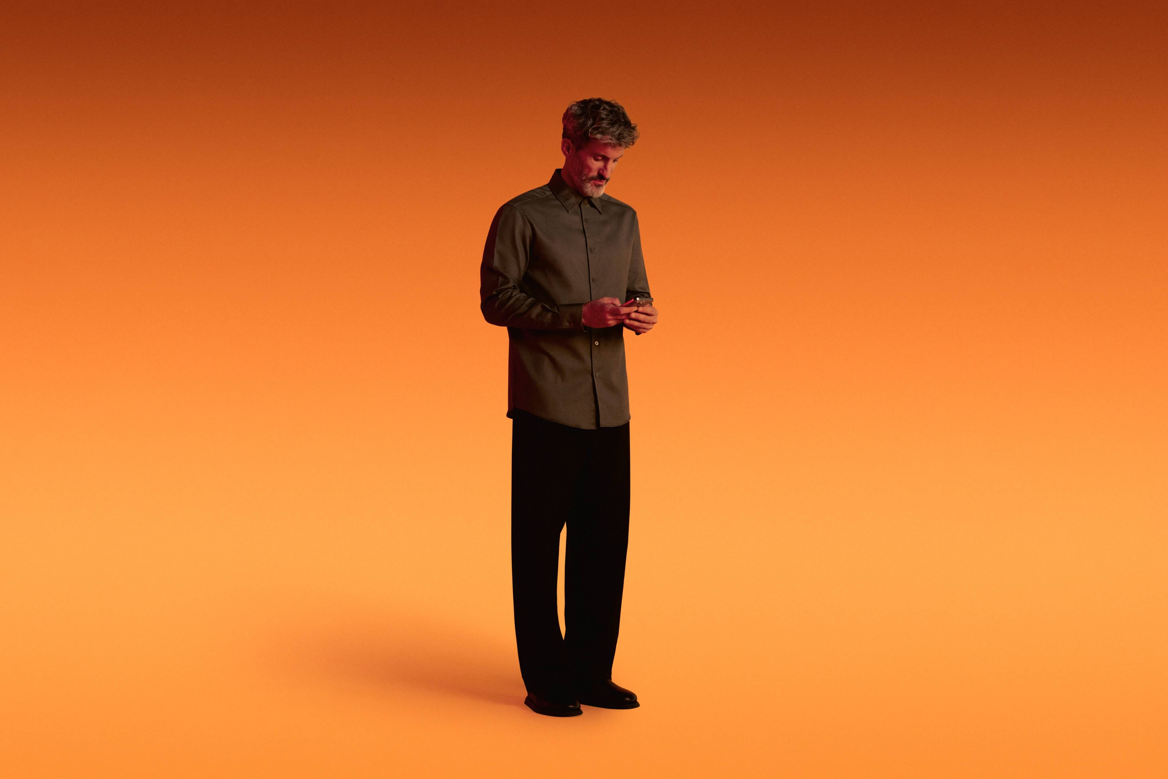 Standing gentleman engaging with the Xapo Bank app on his mobile phone, overlaid with an orange hue.