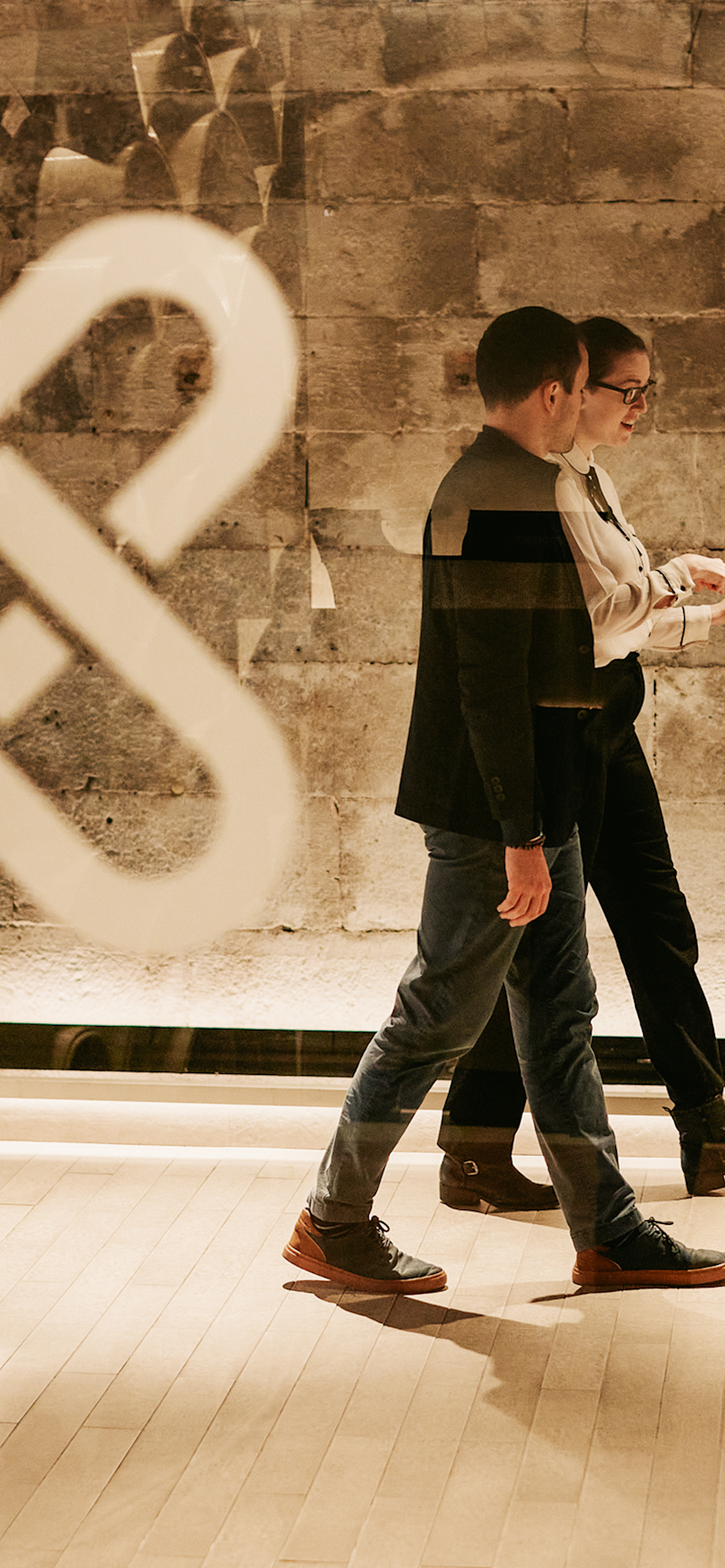 Two colleagues walking and conversing inside the modern Xapo office building, highlighting contemporary corporate workspace design, company branding, and collaborative professional lifestyle.