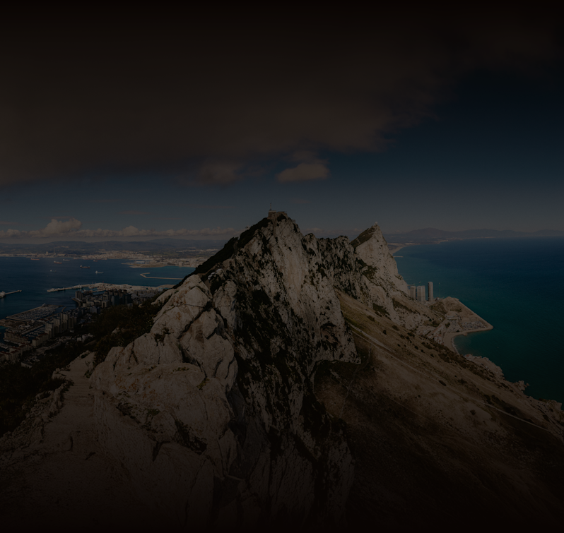 Moody landscape photography of the famous Rock of Gibraltar peninsula, highlighting the steep cliffs overlooking the Strait of Gibraltar and the surrounding port city.