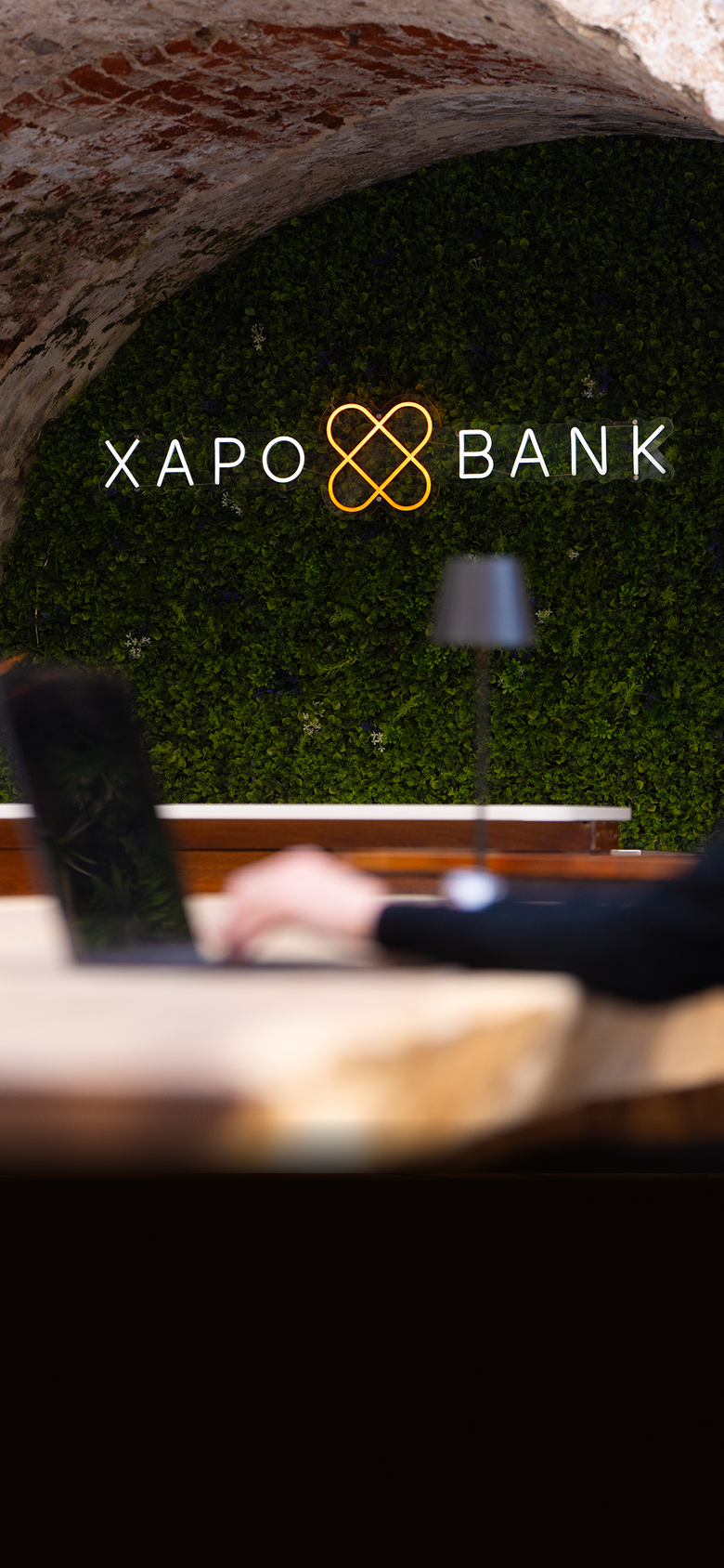 Interior view of the Xapo corporate building, featuring a historic light stone facade adorned with the modern orange Xapo logo and arched doorways with warm interior lighting.