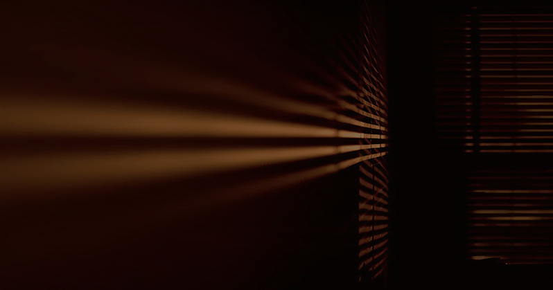 Cinematic dramatic lighting effect with golden light beams filtering through window shutters into a dark, moody interior space, creating high-contrast shadows.