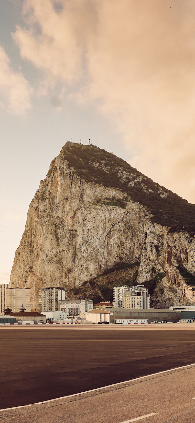 The famous limestone monolith Rock of Gibraltar seen from the airport runway, highlighting the unique landscape where city infrastructure meets the massive Mediterranean headland.